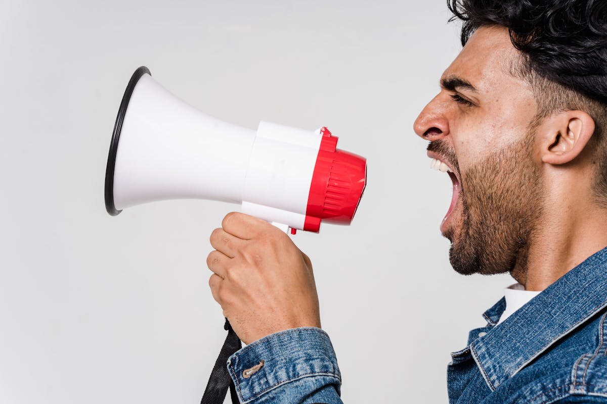 Noise Pollution In China: What Travelers Should Know 7 Close-Up Side View Of A Man Shouting Passionately Into A Megaphone, Expressing Urgency.